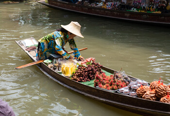 Obraz premium top view asian thai old woman Selling fruit on a boat in a very popular Central Thai traditional floating market, causing many tourists to come and visit.