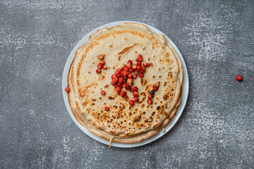 Pancakes and wild strawberries on a plate, top view, isolated on gray textured background.