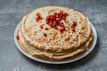 Pancakes and strawberries on a plate, 45 degree tilt view, isolated on grey textured background.