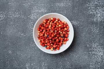 wild strawberries on a plate, top view, on a gray textured background.