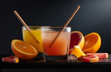 Glasses of grapefruit and orange juice with ice on a black background.