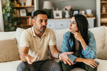 Unhappy couple suffer from problems in relationship, sitting on sofa and arguing