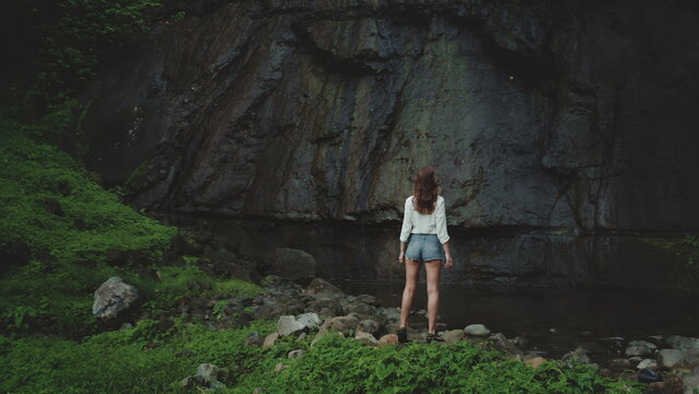 Joyful woman stands in a tropical jungle, gazing at a hidden waterfall, surrounded by lush greenery. This picturesque scene inspires wanderlust