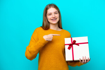 Teenager Russian girl holding a gift isolated on blue background and pointing it