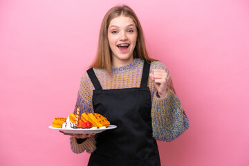 Teenager Russian girl holding a waffles isolated on pink background celebrating a victory in winner position