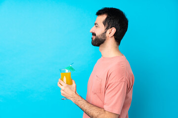 Fototapeta premium Young man over holding a cocktail over isolated blue background in lateral position