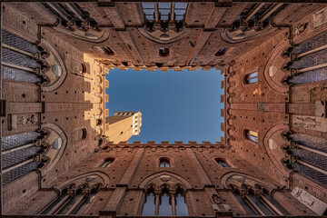 Obraz premium Bottom up view courtyard Palazzo Pubblico gothic heritage building with bell tower, Siena, Italy