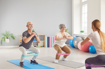 Active happy elderly people, seniors exercising with coach, using fitness rubber band, health care of elderly people, female geriatric instructor helping old woman, man caring for physical well-being