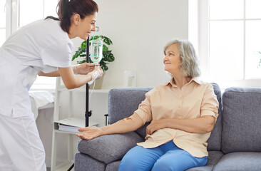 Senior woman with intravenous drip sitting on couch, physician, nurse doctor fixing IV drip infusion, geriatrics hospital eldercare, therapy to infuse vitamins, chemotherapy to maintain health clinic