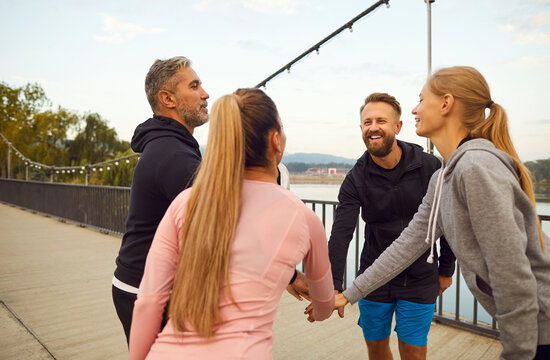 Group of athletes people standing in a circle, holding hands together and showing unity during workout session outdoor. Teamwork, friendship, and the spirit of sportsmanship in fitness and training. - Powered by Adobe