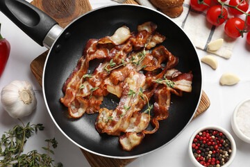 Delicious bacon slices in frying pan and products on white tiled table, flat lay