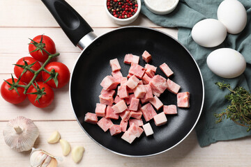 Pieces of fresh bacon in frying pan and products on light wooden table, flat lay