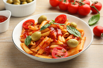 Delicious pasta with tomato sauce, basil and olives in bowl on wooden table, closeup