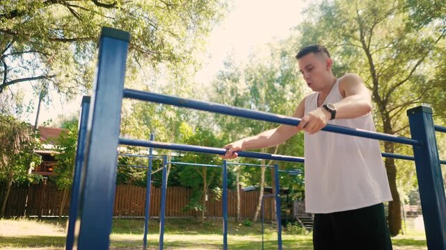 Handsome pumped up young male bodybuilder doing exercises on horizontal bar and parallel bars outdoors on the street. Beautiful male body shapes, beauty and health, training and motivation