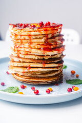 American homemade pancakes with strawberry and lingonberry sauce on a blue plate and berries on a white table.