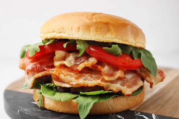 Delicious burger with bacon, tomato and greens on light background, closeup