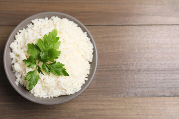 Bowl of delicious boiled rice with parsley on wooden table, top view. Space for text