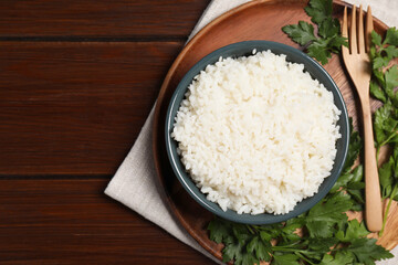 Delicious boiled rice served with parsley on wooden table, top view. Space for text