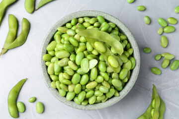 Fresh edamame soybeans in bowl and pods on grey textured table, flat lay