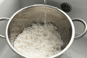 Pouring water into colander with rice in sink, closeup