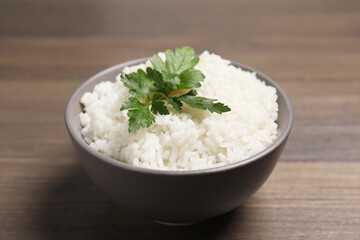 Bowl of delicious boiled rice with parsley on wooden table, closeup