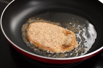 Cooking schnitzel in frying pan on stove, closeup