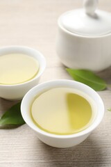 Refreshing green tea in cups and leaves on wooden table, closeup
