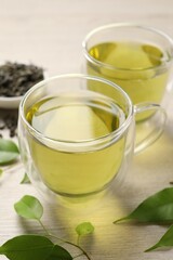 Refreshing green tea in cups and leaves on wooden table, closeup
