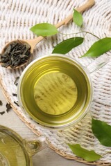 Refreshing green tea in cup, spoon and leaves on table, flat lay
