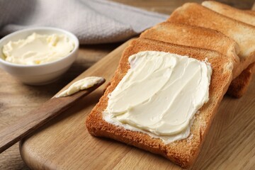 Delicious toasted bread slices with butter and knife on wooden table, closeup