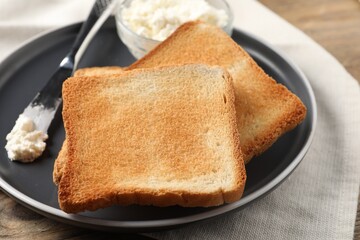 Delicious toasted bread slices with cream cheese and knife on table, closeup