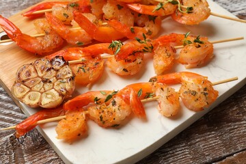 Delicious grilled shrimp skewers and garlic on wooden table, closeup