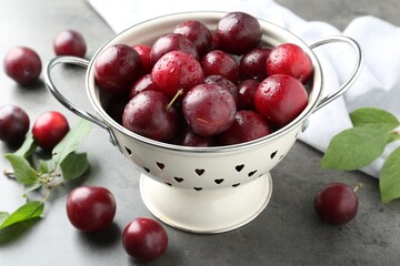 Tasty ripe plums in colander on grey table, closeup