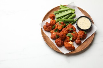 Baked cauliflower buffalo wings with celery and sauce on white table, top view. Space for text