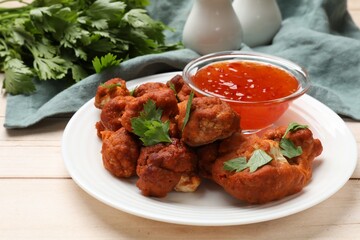 Baked cauliflower buffalo wings with parsley and sauce on wooden table, closeup