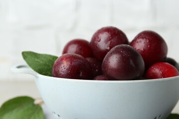 Ripe plums in colander on table, closeup