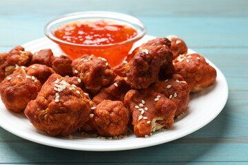 Tasty cauliflower buffalo wings and sauce on light blue wooden table, closeup