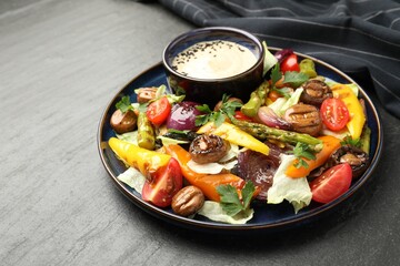 Delicious salad with grilled vegetables and sauce on dark gray textured table, closeup. Space for text