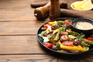 Delicious salad with grilled vegetables and sauce on wooden table, closeup. Space for text