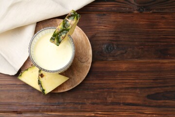 Tasty pineapple smoothie in glass and slices of fruit on wooden table, top view. Space for text