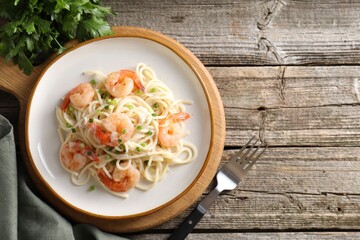 Delicious pasta with shrimps, green onions and parsley on wooden table, top view. Space for text
