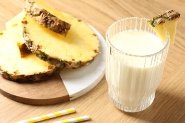 Tasty pineapple smoothie in glass and fresh fruit on wooden table, closeup