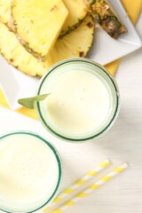 Tasty pineapple smoothie in glasses and fresh fruit on white wooden table, top view