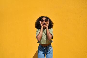 Excited surprised young gen z African American hipster girl wearing sunglasses screaming with open...