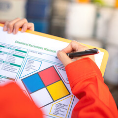 Extreme close-up at industrial worker'hand during verify on chemical and hazard material checklist,...