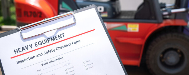 A mechanical engineer is using heavy equipment checklist form for inspecting the factory forklift vehicle (as blurred background). Industrial working with safety practice concept, selective focus.  © Nattawit