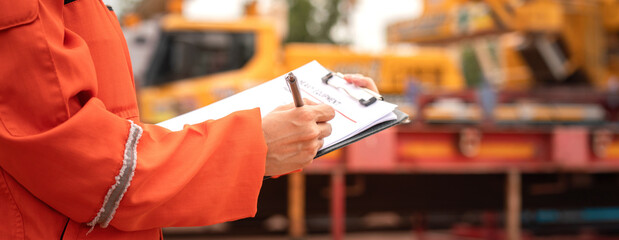 Close-up at the operation supervisor is checking on heavy machine and equipment checklist form with...
