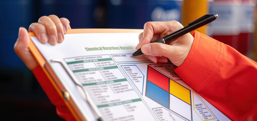 Extreme close-up at industrial worker'hand during verify on chemical and hazard material checklist,...