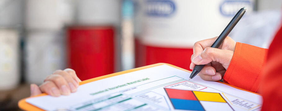 Extreme close-up at industrial worker'hand during verify on chemical and hazard material checklist, with background of chemical storage place. Industrial working with safety practice scene.