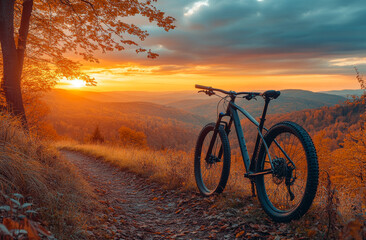 Fototapeta premium Sunset view with a mountain bike on a forest trail in autumn. A mountain bike rests on a scenic trail as the sun sets over autumn foliage.
